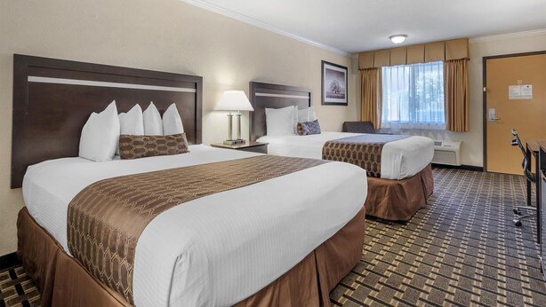 A hotel room with two beds, a desk, a chair, a lamp, and a window with curtains. - Best Western Plus Inn of Hayward (Hayward)