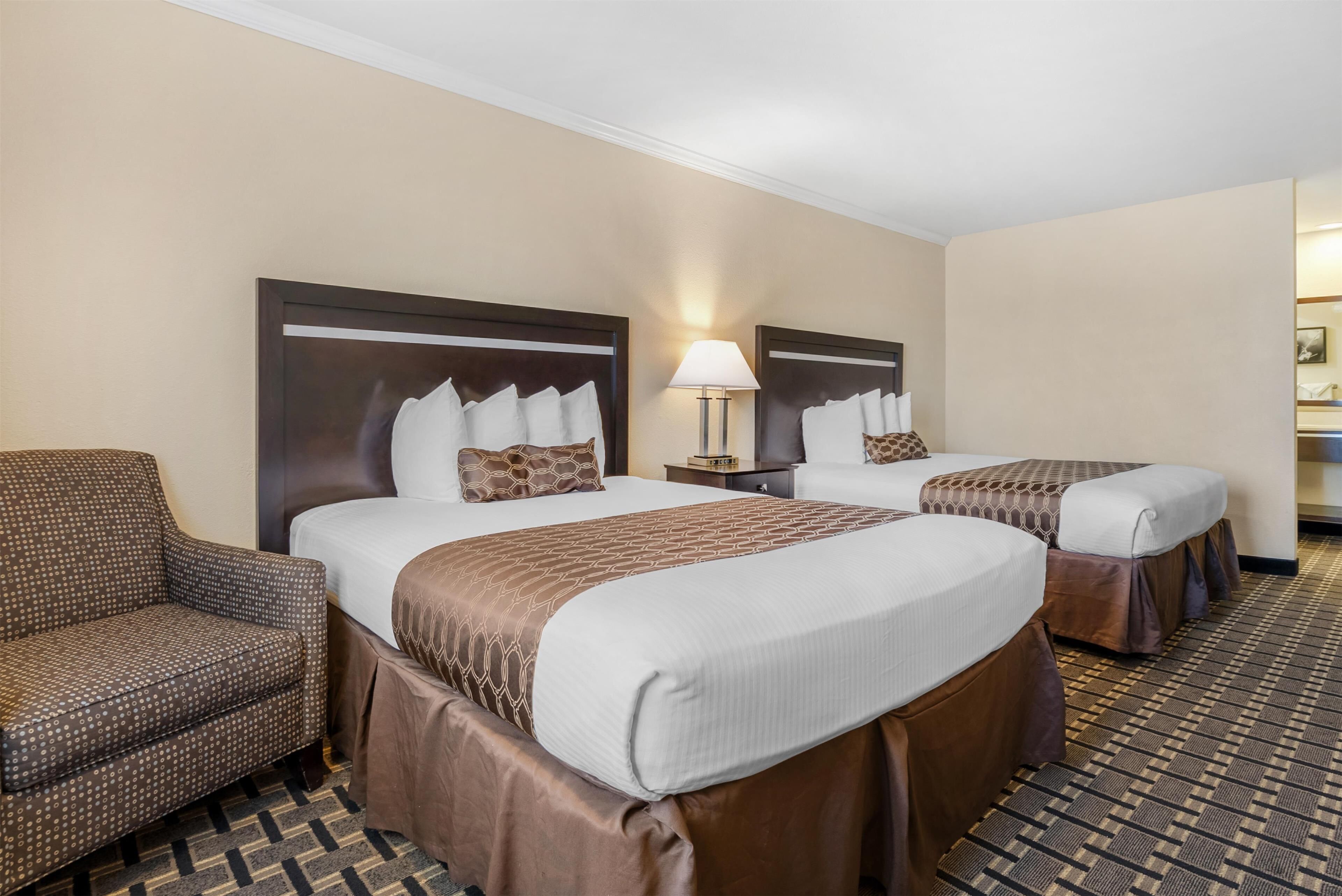 A hotel room with two beds, a sofa, and a nightstand with a lamp.