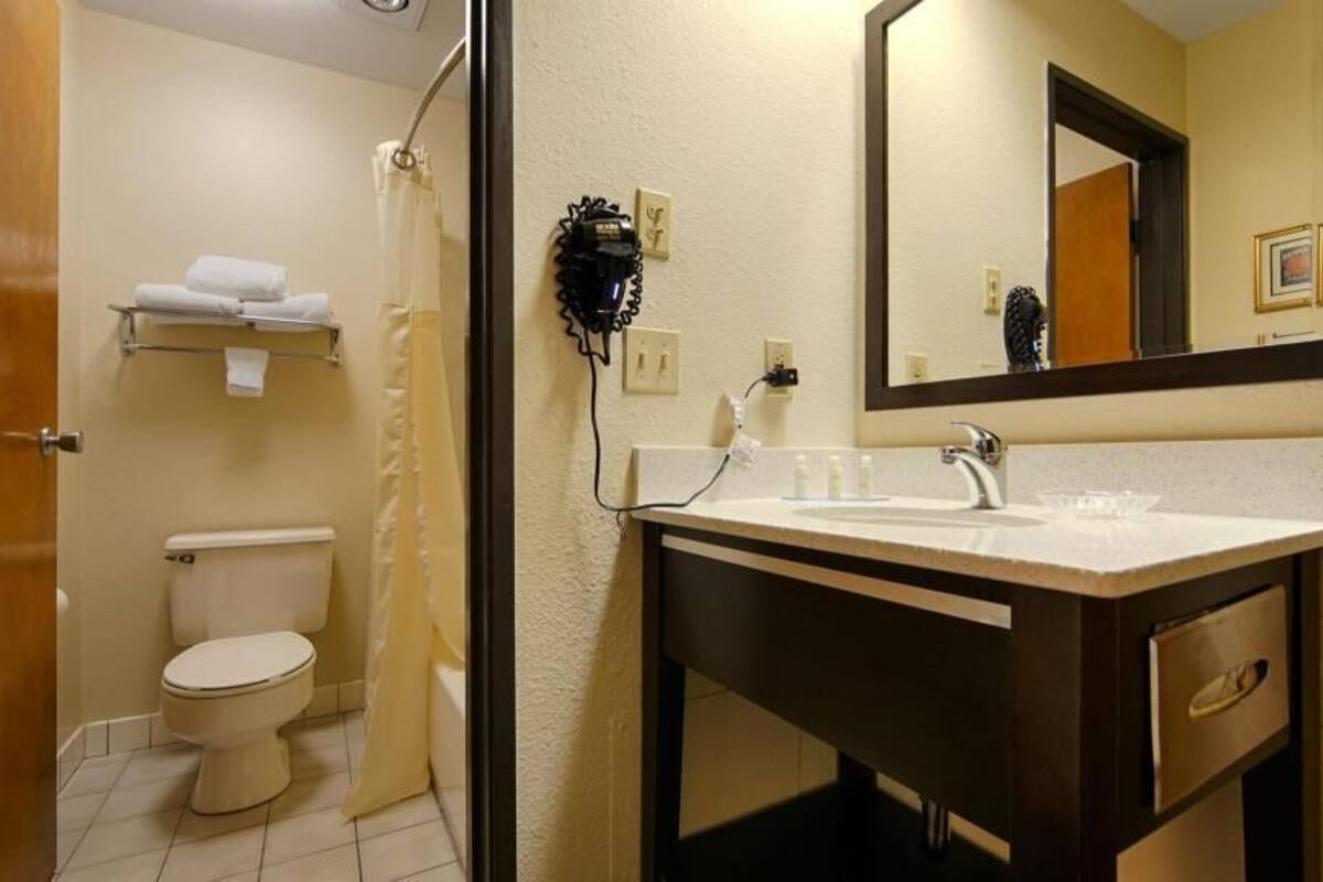 Une salle de bain équipée de toilettes, d’un lavabo, d’un miroir et d’un sèche-cheveux fixé au mur.