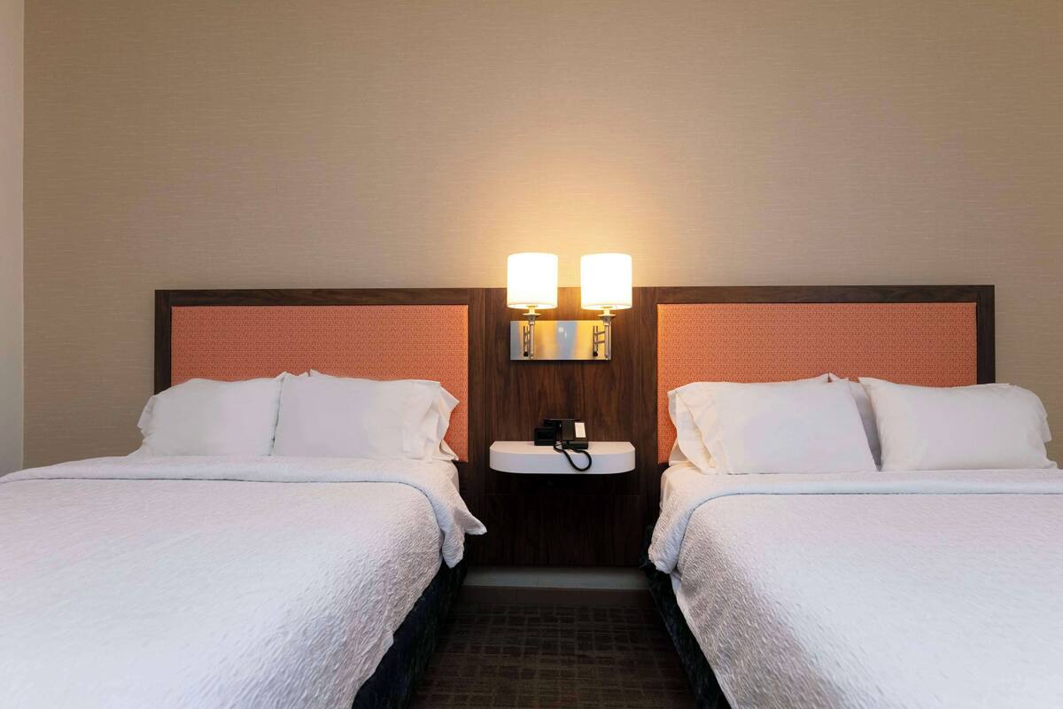 A hotel room with two beds, a wooden headboard, a white sink, and two wall-mounted lights.