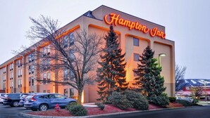 Un hotel Hampton Inn amb façana moderna, pàrquing i arbres als voltants.