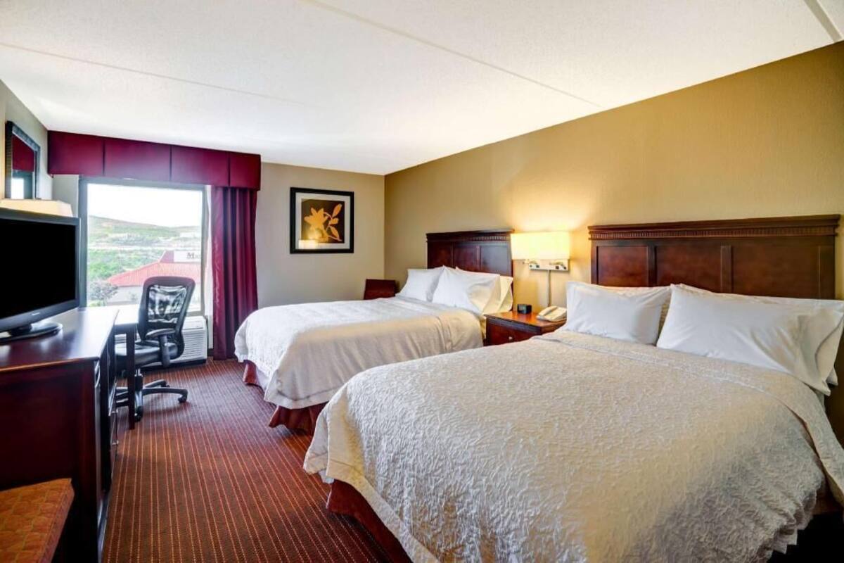 A hotel room with two beds, a desk with a TV, a chair, a lamp, and a window with a view.