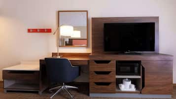Habitación de hotel con un escritorio de madera, una silla de oficina negra, un televisor de pantalla plana, un microondas y una pequeña zona de kitchenette.
