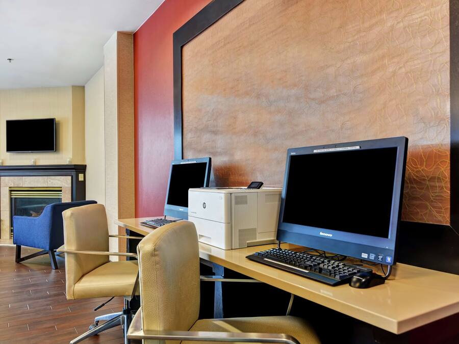 Habitación de hotel con escritorio, dos monitores, una impresora y un televisor de pantalla plana montado en la pared.