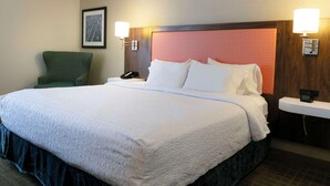 A hotel room with a large bed, a green armchair, and two bedside tables with lamps.