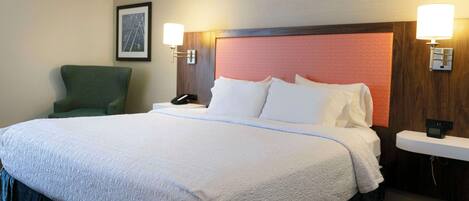 A hotel room with a large bed, a green armchair, and two bedside tables with lamps.