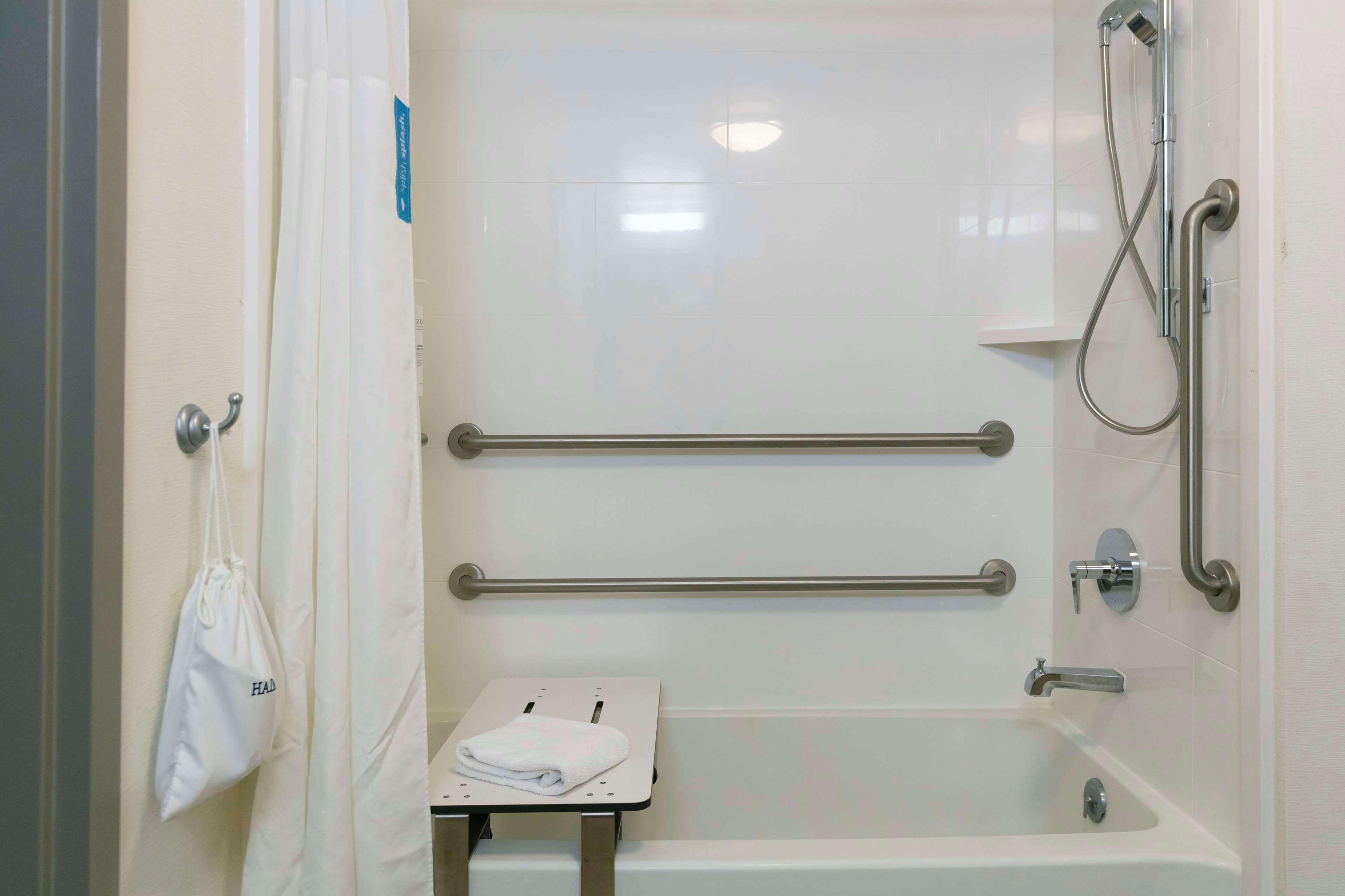 A bathroom with a bathtub, grab bars, a towel rack, and a small table with a towel.