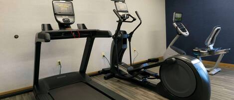 A fitness room with treadmills, elliptical machines, and wall-mounted screens.