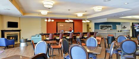 A hotel dining area with multiple tables and chairs, a fireplace, and a television mounted on the wall.