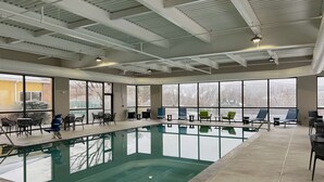 An indoor swimming pool with clear glass walls, surrounded by seating areas and large windows.