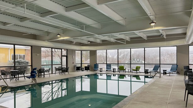 Una piscina interior amb parets de vidre transparent, envoltada d'espais d'seure i grans finestres.