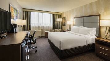 A hotel room with a bed, desk, chair, and TV.