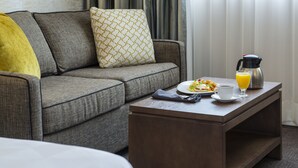 A modern living room with a grey sofa, a wooden coffee table, and a breakfast setup including eggs benedict, orange juice, and a coffee pot.