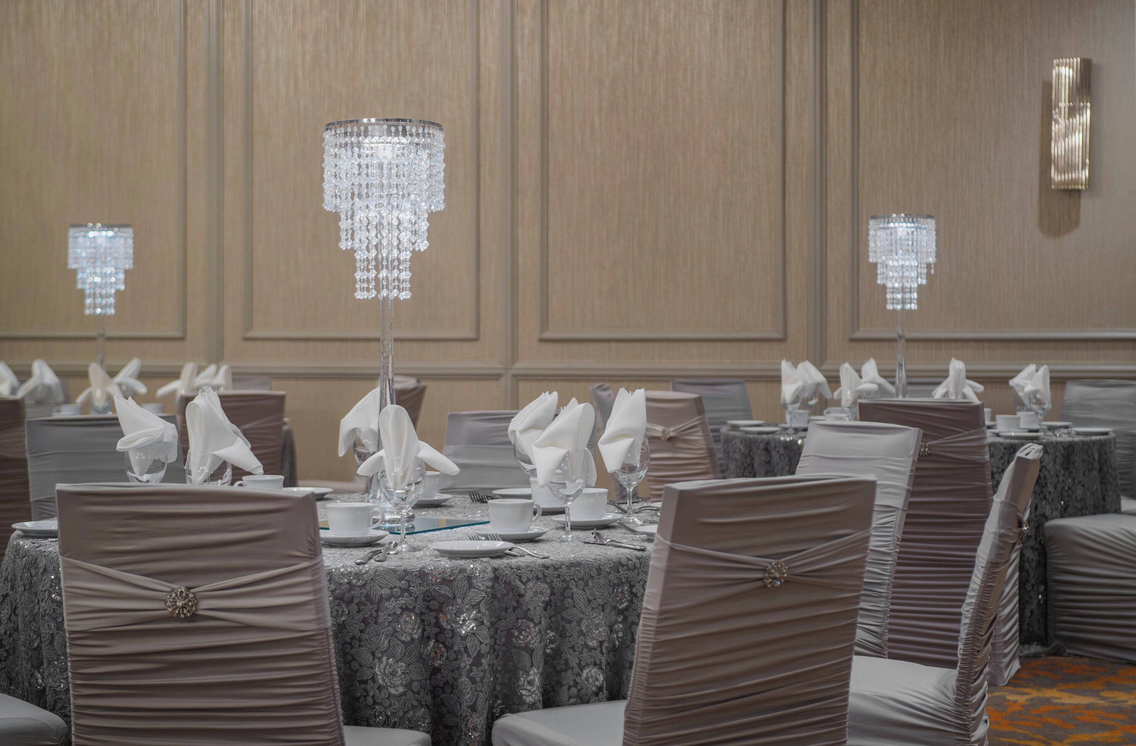 A banquet hall with tables set for a formal event, featuring crystal chandeliers and neatly arranged table settings.