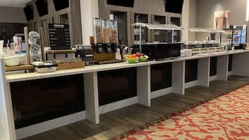 Montaje de bufé con varias estaciones de comida, incluyendo una barra de café, una barra de ensaladas y una sección de alimentos calientes.
