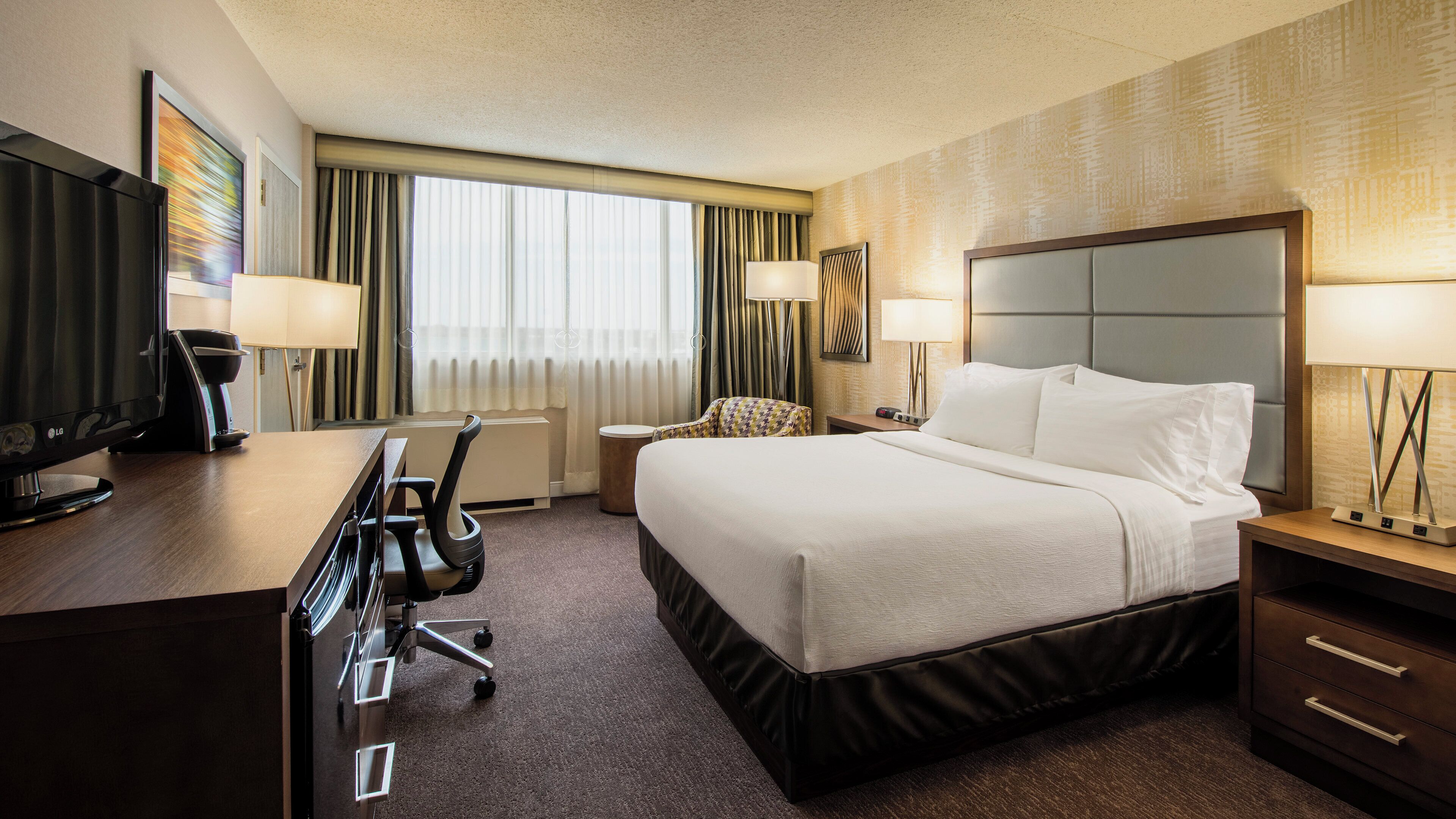 A hotel room with a bed, desk, chair, television, and lamps.