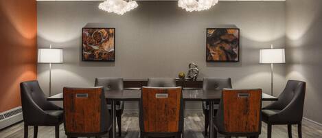 Un salón de conferencias con una mesa rectangular, seis sillas, dos lámparas fijadas a la pared y dos cuadros abstractos.