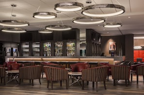 A bar area with multiple seating options, a counter with a variety of bottles, and a modern ceiling design. - Holiday Inn Winnipeg South by IHG (Winnipeg)