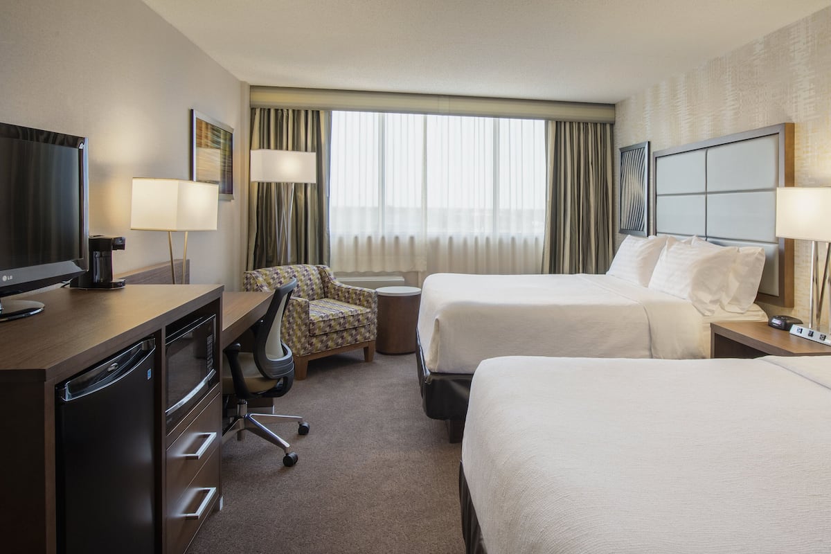 A hotel room with two beds, a desk with a television, a chair, and a lamp.