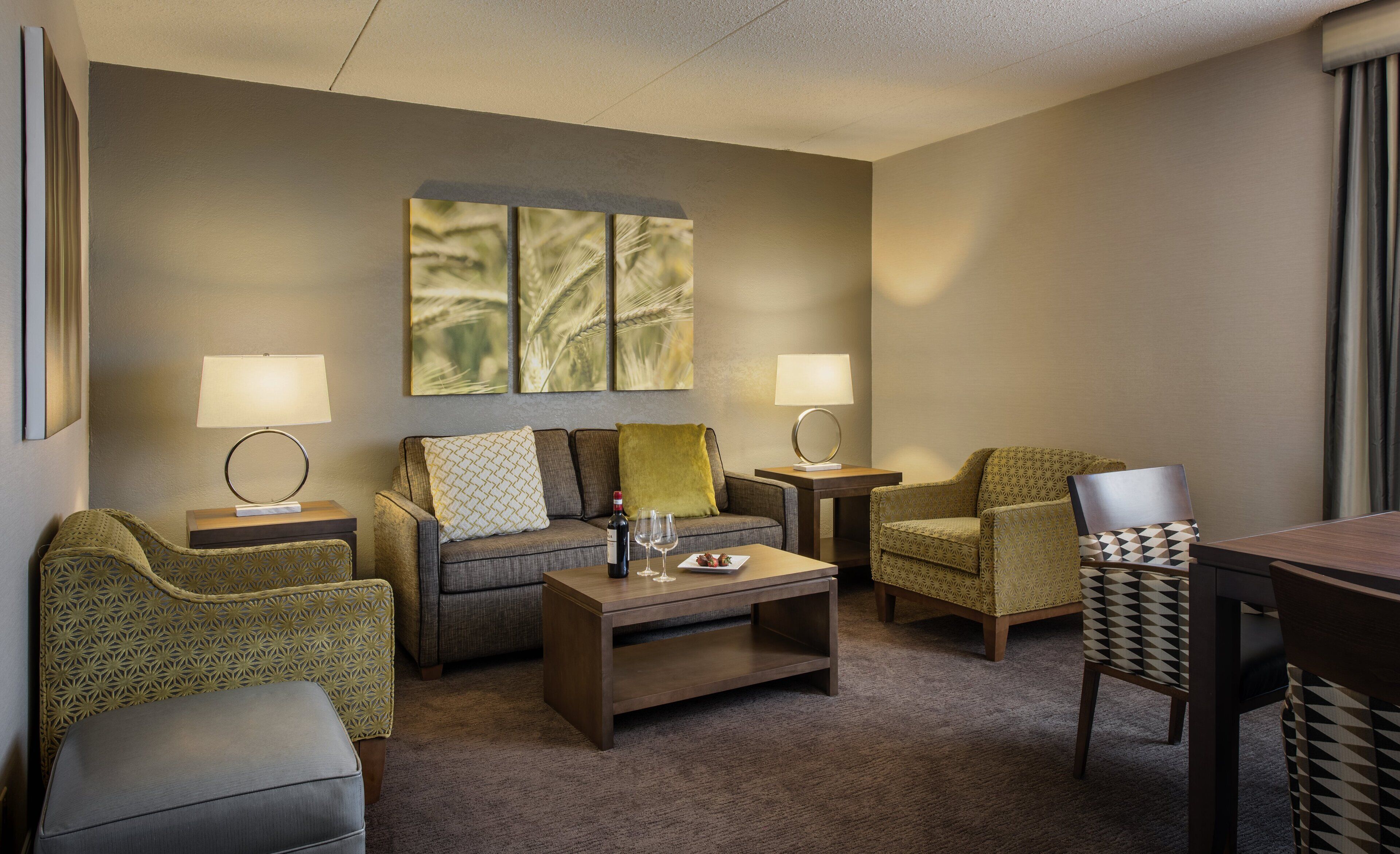 A hotel room with a sofa, armchairs, a coffee table, and two lamps.