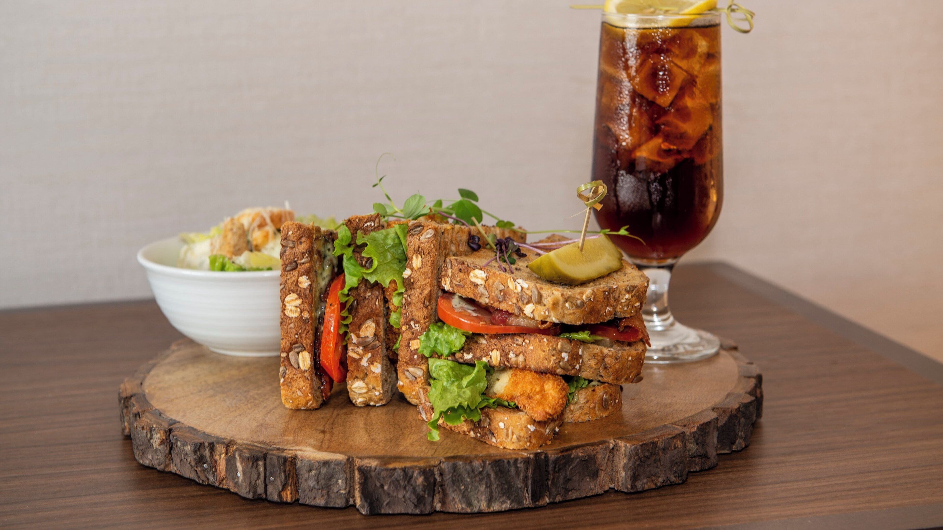 A sandwich on a wooden board with a drink in the background.