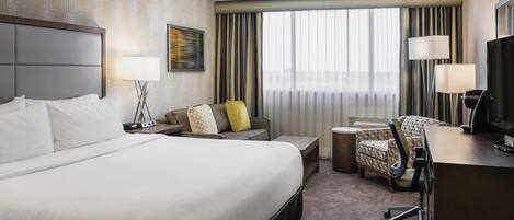 A hotel room with a large bed, a desk, a chair, a small table, and a TV.