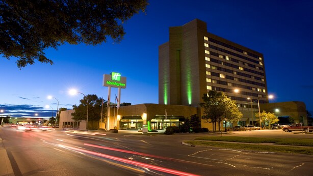 A Holiday Inn hotel with a prominent sign, a parking lot, and a multi-story building with illuminated windows. - Holiday Inn Winnipeg South by IHG (Winnipeg)