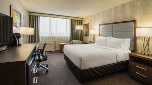 A hotel room with a bed, desk, chair, TV, lamps, and a window with curtains. - Holiday Inn Winnipeg South by IHG (Winnipeg)