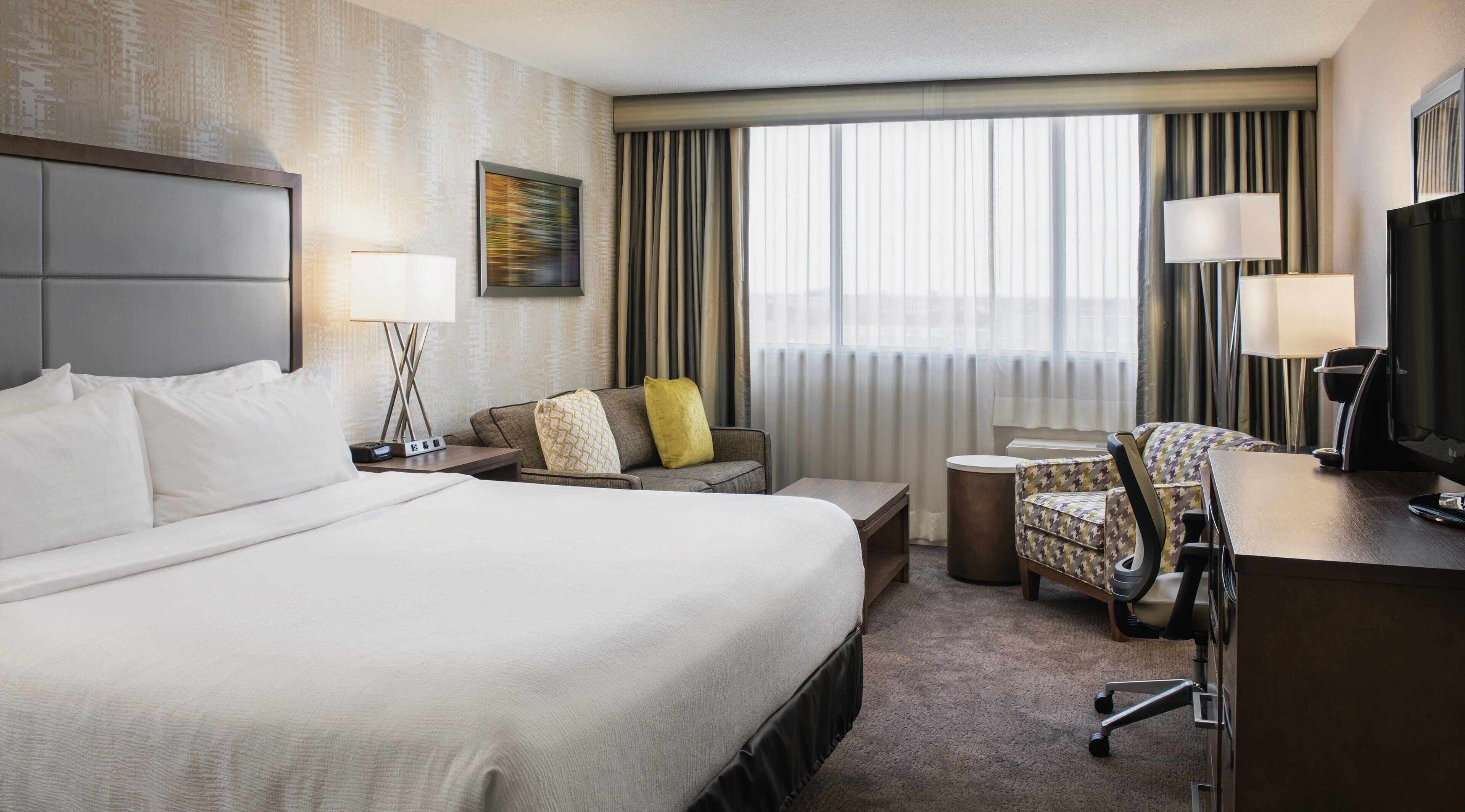 Une chambre d’hôtel avec un grand lit, un bureau, une chaise, un canapé et un téléviseur.