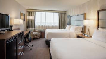 Une chambre d’hôtel avec un lit, un bureau avec une télévision, une chaise et une fenêtre avec des rideaux.