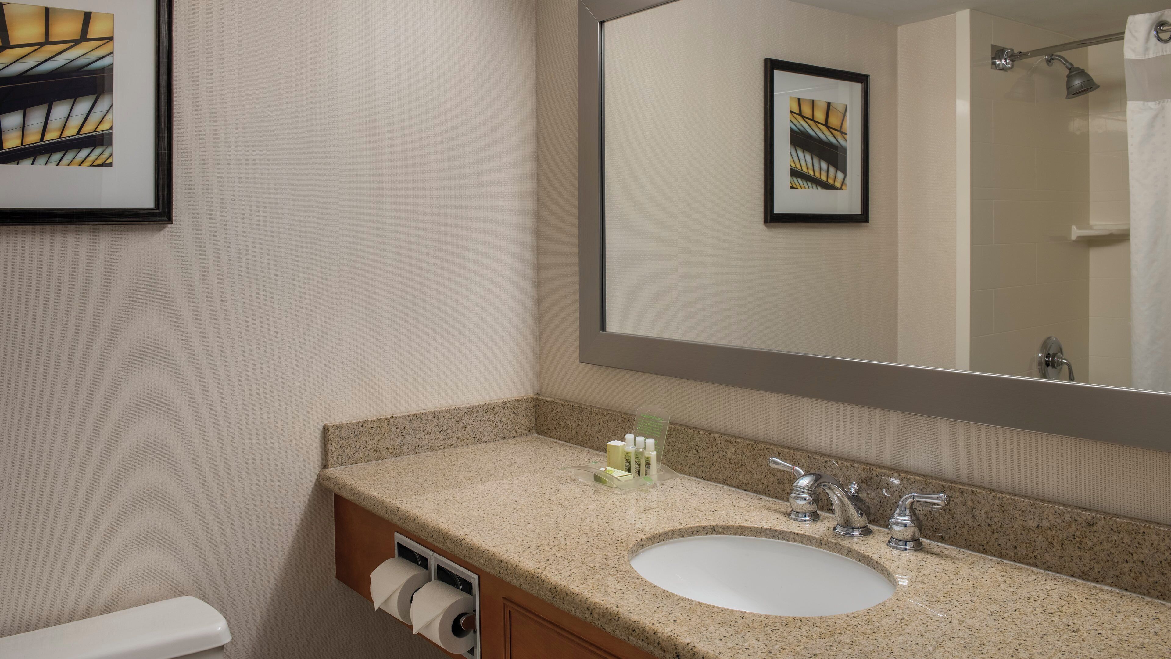 A bathroom with a granite countertop sink, a mirror, and a toilet.