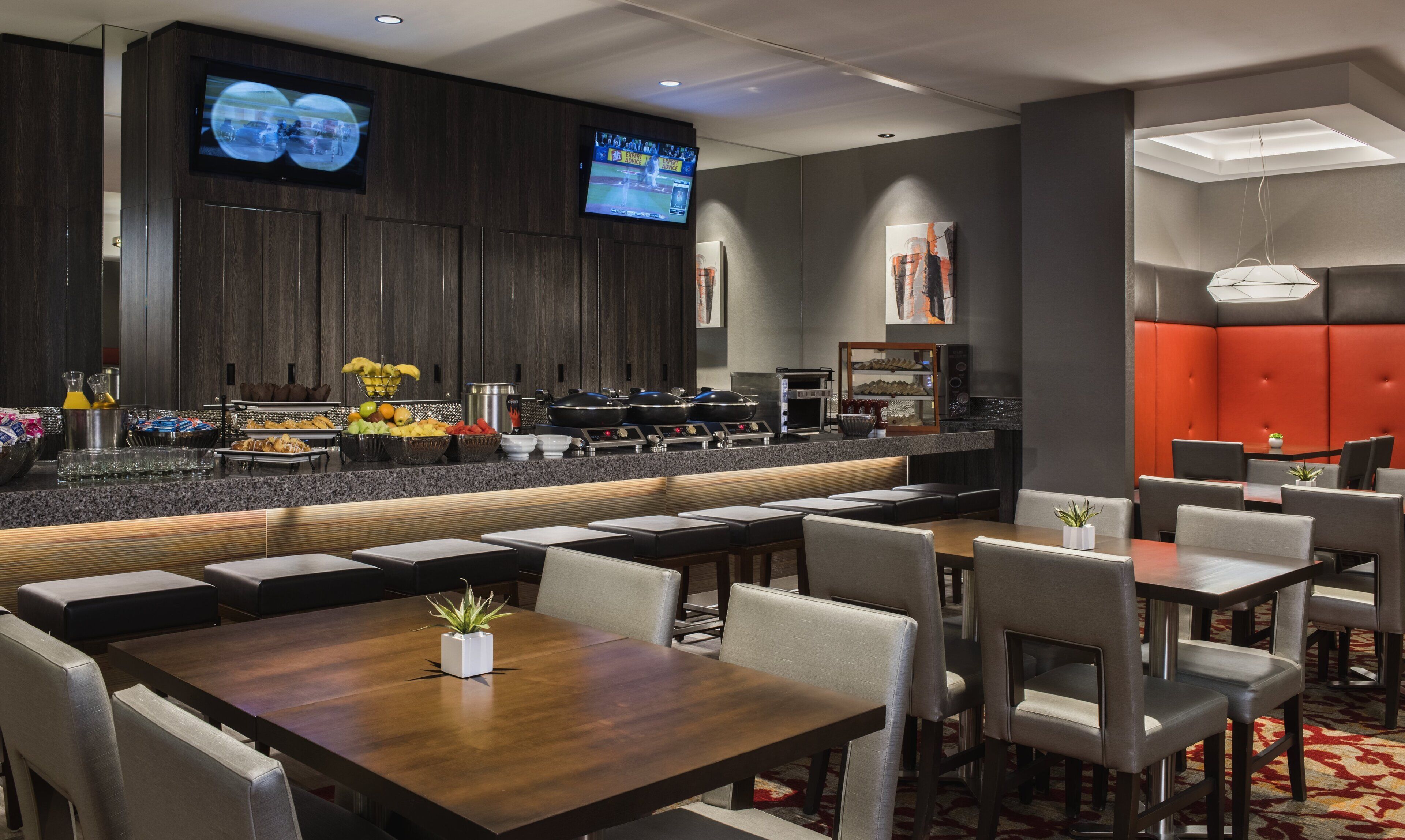 Un moderno vestíbulo de hotel con zona de bar, asientos y una televisión mostrando un evento deportivo.