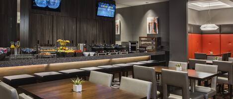 A modern hotel lobby with a bar area, seating, and a television displaying a sports event.