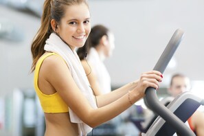 A person using an exercise machine in a gym with other people in the background. - Holiday Inn Winnipeg South by IHG (Winnipeg)