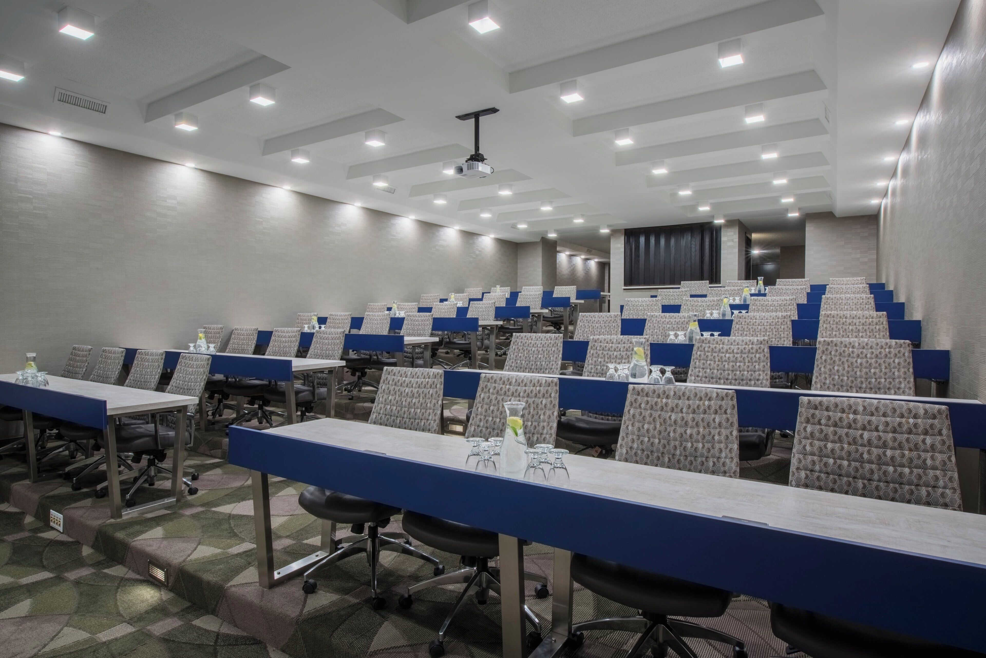 A conference room with rows of tables and chairs, equipped with water bottles and glasses.