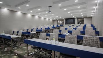 A conference room with rows of tables and chairs, equipped with water bottles and glasses.