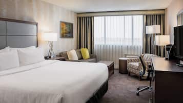 Habitación de hotel con una cama grande, un escritorio con silla, televisión y ventana con cortinas.