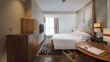 A hotel room with a bed, bedside table, TV, and a desk with a chair.
