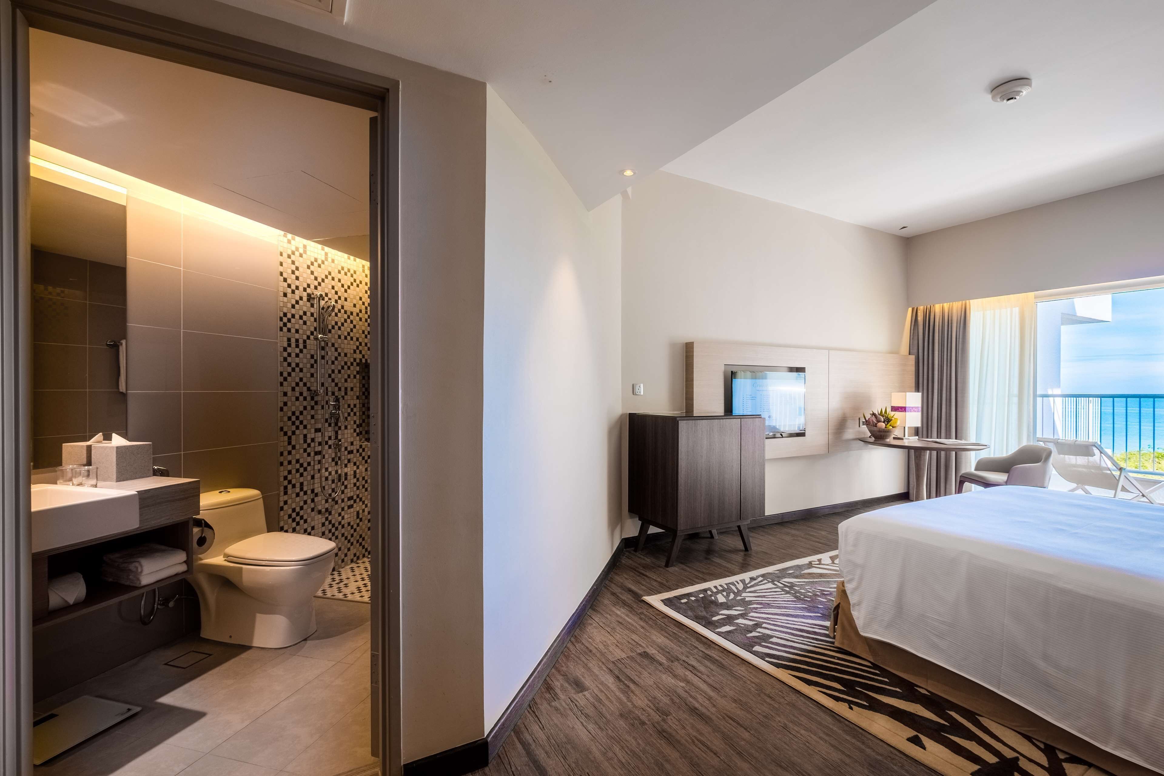 A hotel room with a large bed, a desk with a computer, a TV, and a view of the outdoors.