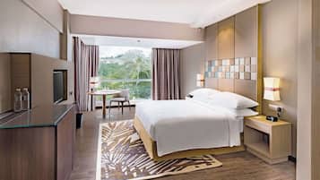 Habitación de hotel con cama, mesitas de noche, escritorio, silla, televisor y vistas al exterior.