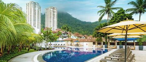 A swimming pool with lounge chairs and umbrellas, surrounded by palm trees and buildings.