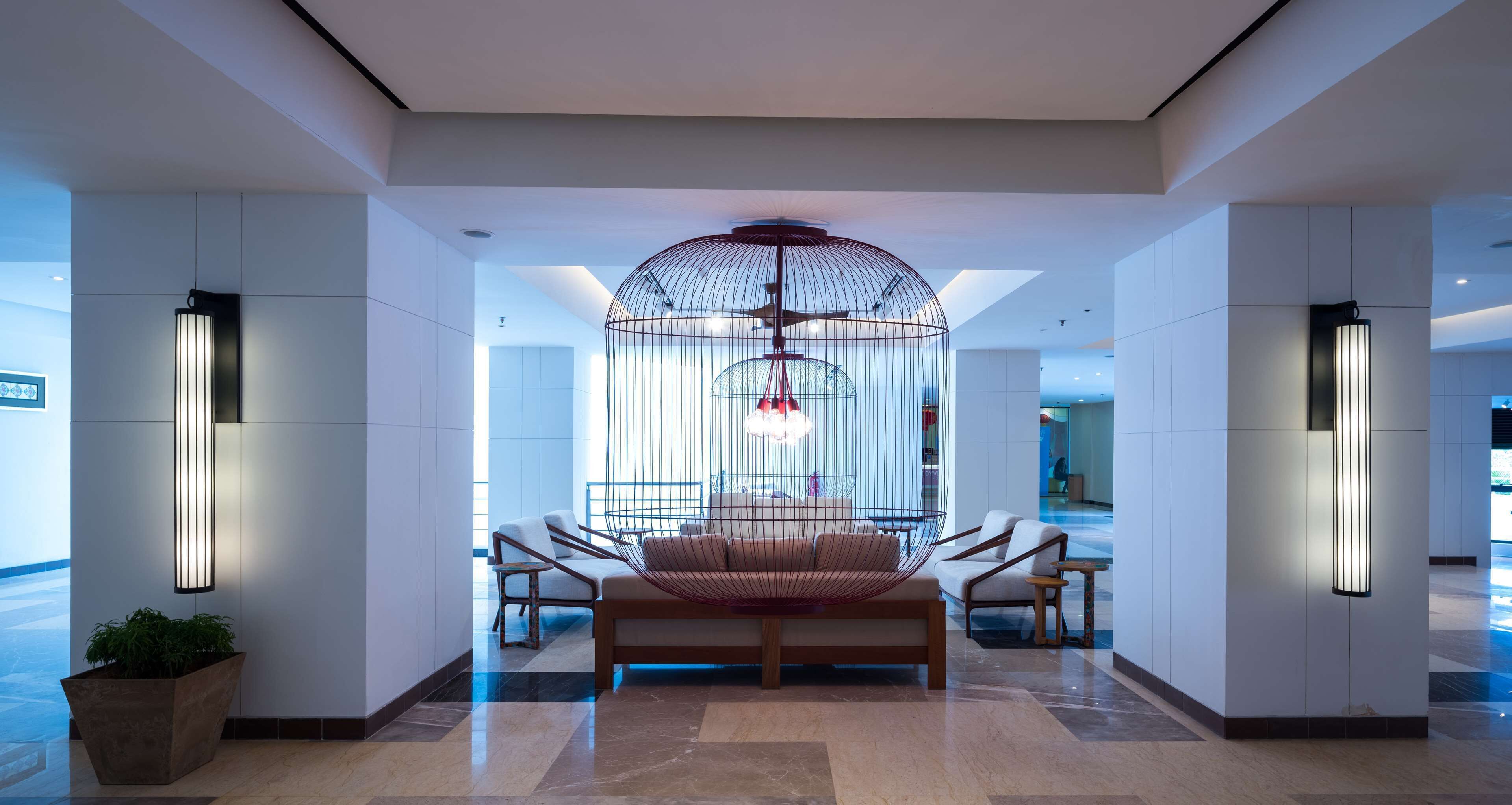 A modern lobby with a central seating area, a large hanging light fixture, and a potted plant.