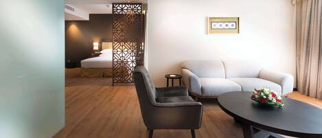 A modern hotel room with a bed, a sofa, a chair, and a round table with flowers.