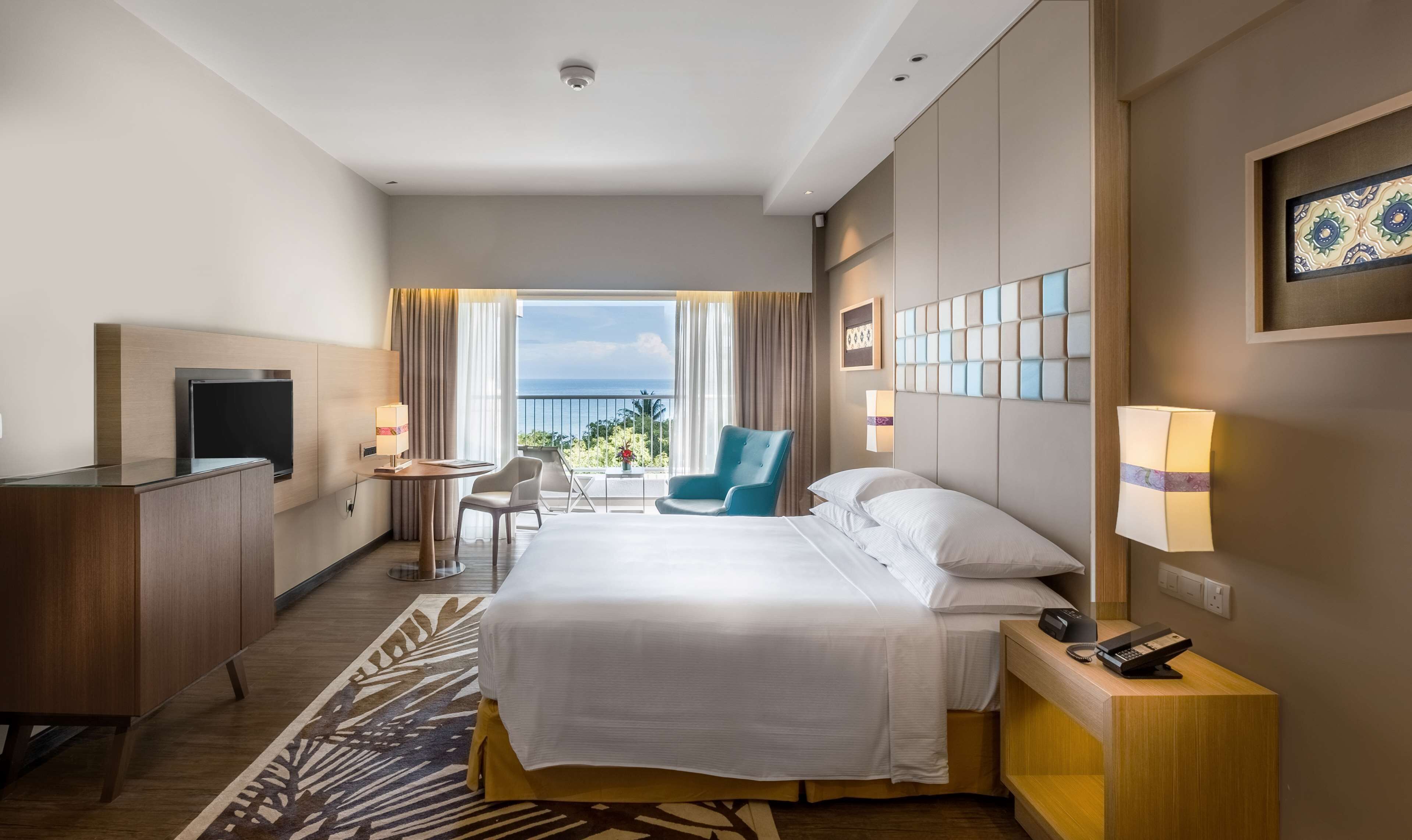 Habitación de hotel con cama, escritorio, silla, televisor y vista al océano.