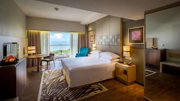 A hotel room with a bed, desk, chair, and a view of the sea.
