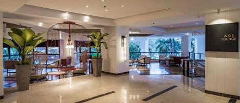 Un área de lounge moderna con asientos, plantas grandes en macetas y un letrero que dice "AXIS LOUNGE".