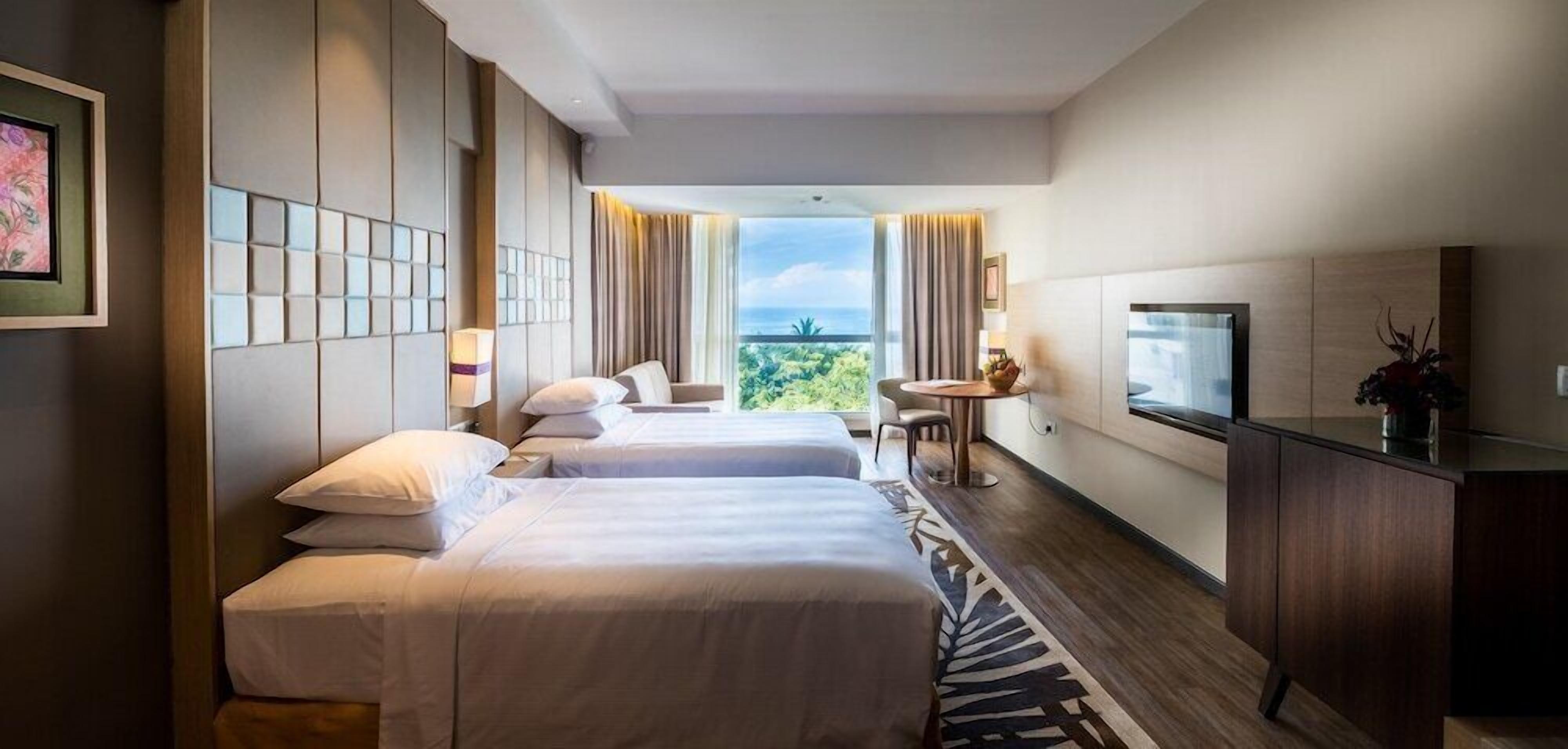 A hotel room with two beds, a TV, a small table, and a view of the outdoors.