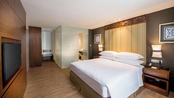 A hotel room with a large bed, bedside tables, a TV, and a bathroom visible through a glass partition.