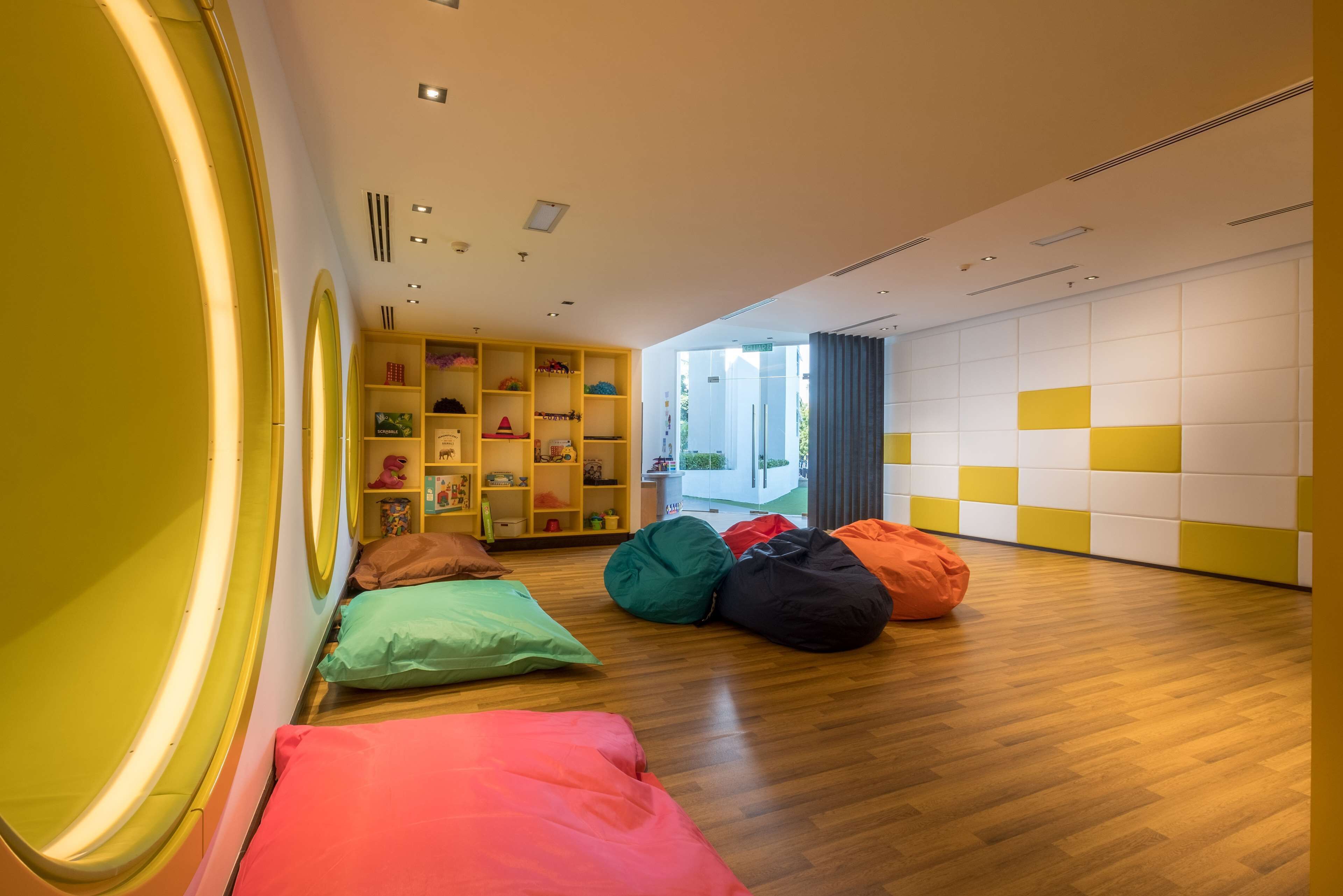 A brightly lit room with wooden flooring, colorful bean bags, and a yellow and white wall with a geometric pattern.
