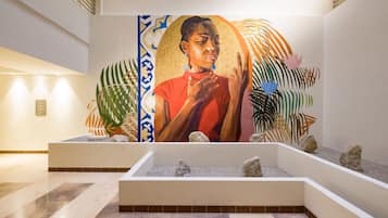 A lobby with a large mural, a reception desk, and a seating area with plants and rocks.